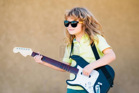 Téléchargez les photos : Garçon avec guitare. Enfant joue une guitare et chante, musique pour enfants et chanson - en image libre de droit