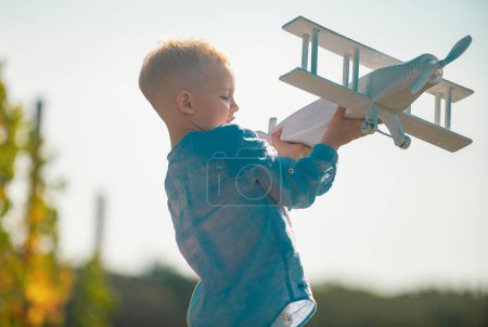 Foto de Niño piloto con juguete avión sueña con viajar en verano en la naturaleza. Los niños sueñan. El niño juega con un avión de juguete y sueña con convertirse en piloto. Concepto de imaginación de sueño infantil - Imagen libre de derechos