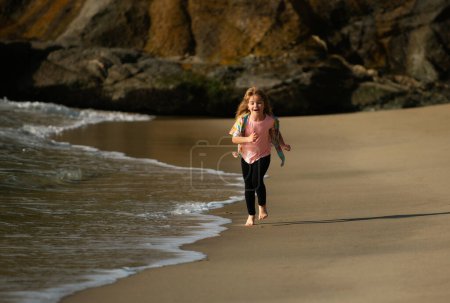 Téléchargez les photos : Des enfants qui jouent sur la plage. Les enfants jouent en mer pendant les vacances d'été en famille. Du sable et de l'eau, de la protection solaire. Petit athlète en entraînement. Exercice du coureur, jogging pour les enfants - en image libre de droit