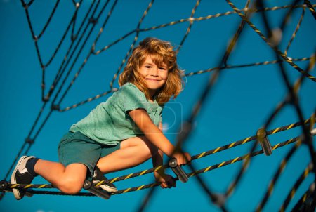Téléchargez les photos : Garçon enfant heureux jouant sur la corde aire de jeux extérieure - en image libre de droit
