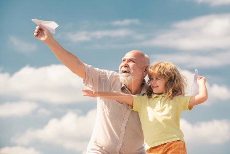 Photo for Grandson child and grandfather with toy paper plane against summer sky background. Child boy with dreams of flying - Royalty Free Image