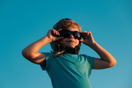 Téléchargez les photos : Enfant drôle ou enfant petit garçon pilote jouer avec des lunettes de pilote et un casque, la liberté de démarrage et insouciant. Rêves de vol. Enfant jouant contre le ciel - en image libre de droit