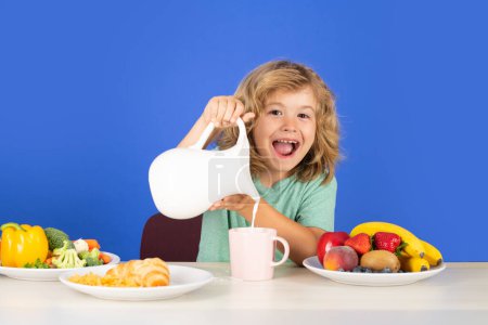 Téléchargez les photos : Enfant excité ayant un petit déjeuneret verser du lait. Un enfant boit du lait. Enfant versant du lait, portrait isolé en studio - en image libre de droit