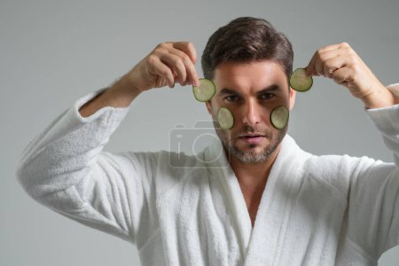 Téléchargez les photos : Beauté homme tenir concombre pour masque de cosmétologie. Homme d'âge moyen avec concombre isolé sur fond de studio. Concombre pour masque cosmétique. Masque facial au concombre - en image libre de droit
