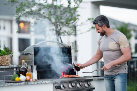 Photo for Handsome male preparing barbecue, grill outdoors. Man cooking meat and fish on barbecue in the backyard. Grill cook. Cooking barbecue. Preparing food on grill using a barbecue set - Royalty Free Image