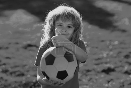 Foto de Niño jugando al fútbol, niño feliz disfrutando del juego de fútbol deportivo, actividades infantiles, pequeño jugador de fútbol. Activo deportivo espectáculo de fútbol para niños pulgares hasta signo de éxito - Imagen libre de derechos