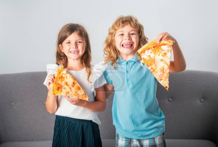 Foto de Dos niños comiendo pizza y sonriendo dentro. Feliz sonrisa niños sosteniendo pizza rebanada cerca de la cara - Imagen libre de derechos
