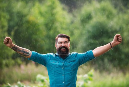 Foto de Tormentoso concepto de tiempo lluvioso. Ropa impermeable. Feliz hombre bajo la lluvia. Humor de otoño - Imagen libre de derechos