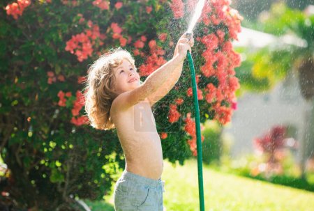 Foto de Divertido niño jugando con manguera de jardín en el patio trasero. Niño divirtiéndose con spray de agua. Actividad al aire libre de verano para niños - Imagen libre de derechos