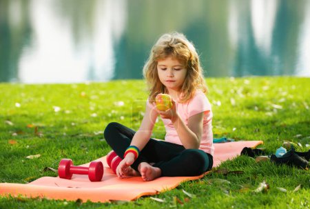 Foto de Niño niño comer manzana relajarse en la alfombra deportiva después de ejercicios deportivos al aire libre en el parque - Imagen libre de derechos