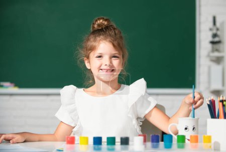 Téléchargez les photos : Petite fille mignonne enfant peinture avec des peintures couleur et pinceau. Cours de dessin à l'école. Éducation de la petite enfance - en image libre de droit