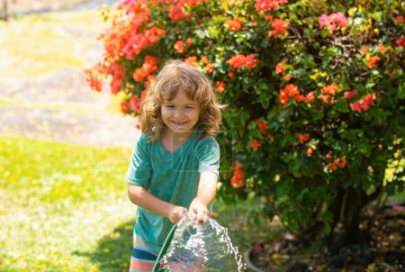 Téléchargez les photos : Enfant garçon arrosant les plantes, de la pulvérisation de tuyau avec tuyau d'eau dans le jardin à l'arrière de la maison un soir d'été - en image libre de droit