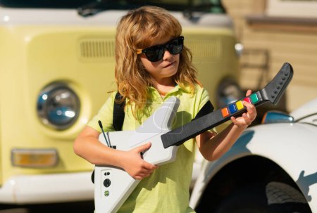 Foto de Niño músico tocando la guitarra como una estrella de rock al aire libre. Niño músico de rock con guitarra. Niño con guitarra - Imagen libre de derechos