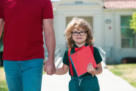 Photo for Parent and nerd pupil of primary school go hand in hand. Father holding hand of son with backpack outdoors, back to school - Royalty Free Image