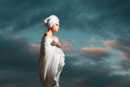 Téléchargez les photos : Femme détendue en peignoir avec serviette sur la tête sentant le café dans la nuit au ciel dramatique en plein air. Spa du matin - en image libre de droit
