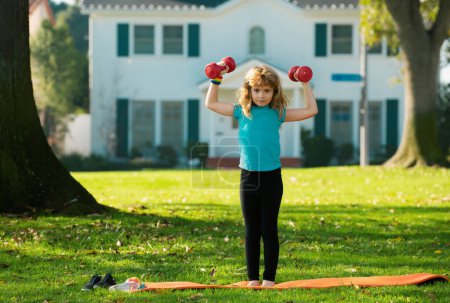 Photo for Child boy working out with dumbbells on park background. Kids sport outdoor - Royalty Free Image