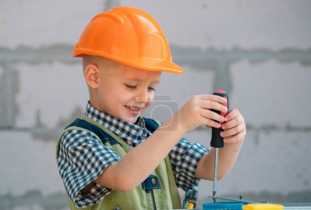 Photo for Little boy holding screwdriver. Kid twists bolt with screwdriver. Little Repairman with repair tool. Cute kid as a construction worker. Childrens play with a hammer pliers and screwdriver. Repair home - Royalty Free Image