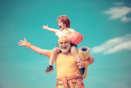 Téléchargez les photos : Homme âgé et mignon petit garçon s'exerçant sur fond de ciel bleu - isolé. Père et fils sportifs - temps en famille ensemble. Faire du sport est gratuit - en image libre de droit