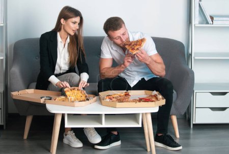 Téléchargez les photos : Des gens d'affaires qui mangent des pizzas. Couple manger de la pizza au bureau - en image libre de droit