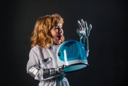 Photo for Cute little boy spaceman child in space suit holding helmet on black background. Child in an astronaut costume plays and dreams of becoming a spaceman - Royalty Free Image