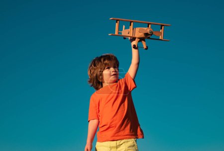 Foto de Niño niño de 7 años jugando con un avión de juguete de madera, sueña con convertirse en piloto. Sueños de niños. Aviador piloto infantil con avión de madera - Imagen libre de derechos