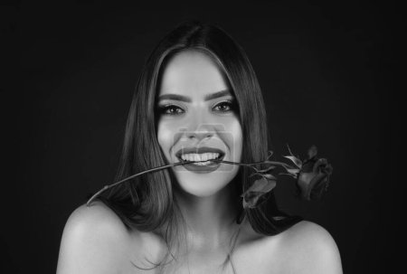 Téléchargez les photos : Rose flowers in a mouth. Beauty romantic woman with rose flowers. Seductive sensual woman holding red rose with teeth. Portrait of fashion model girl on studio background. Birthday day - en image libre de droit