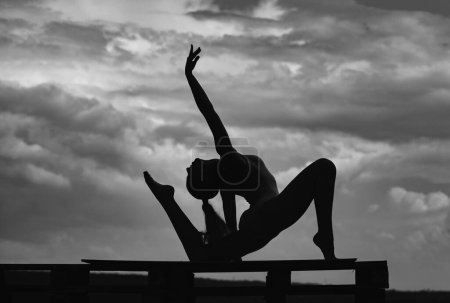 Photo for Yoga woman stretching with pose stretch. Silhouette of fit fitness athlete girl exercising sports stretches. Cloudy sky background - Royalty Free Image