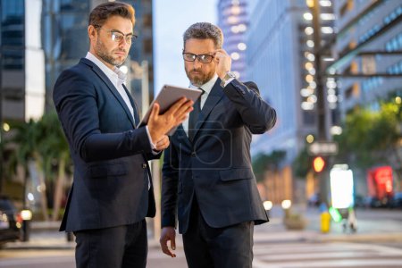 Photo for Business men check their emails and review important documents on tablet on night city background. Business technology. Businessman showing content on tablet to colleague. Night business in city - Royalty Free Image