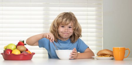 Photo for Schoolchild eating breakfast before school. Hunger, appetite concept. Portrait of little teen child sit at desk at home kitchen have delicious tasty nutritious breakfast - Royalty Free Image