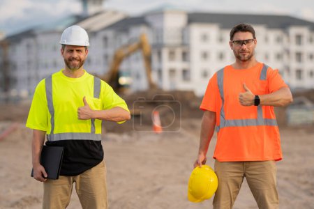 Photo for Construction site workers in a helmet work hard. Two workers in a hard hat is responsible for ensuring safety while constructing buildings. Builders workers personal protective equipment - Royalty Free Image