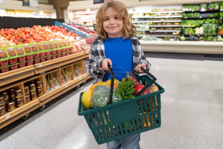 Téléchargez les photos : Portrait d'enfant avec panier plein de légumes frais dans un magasin d'aliments. Supermarché et concept d'épicerie. Faire du shopping. Un enfant achète de l'épicerie au supermarché. tenir le panier - en image libre de droit