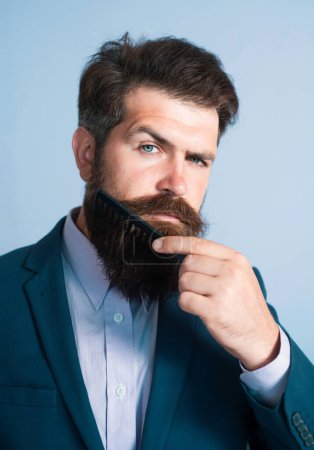Foto de Primer plano de un joven que se peina la larga barba. Cuidado con la barba. Barbudo hombre con barba, barbudo gay. Concepto de barbería. Hombres bigote - Imagen libre de derechos