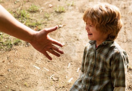 Foto de Un niño pequeño llora en el parque. Los padres apoyan al hijo con la mano. Ayudando con el concepto de mano. Concepto de paternidad - Imagen libre de derechos