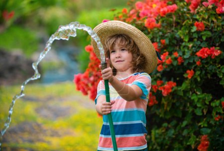 Téléchargez les photos : Joyeux petit garçon qui s'amuse dans le jardin domestique. Tenue enfant arrosage tuyau d'arrosage. Jeux actifs en plein air pour les enfants dans la cour pendant la récolte. - en image libre de droit