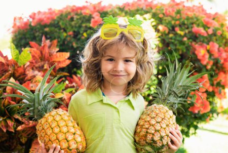 Téléchargez les photos : Jeune garçon drôle tenant l'ananas et souriant dans la cour. Enfant avec ananas. Enfants fruits d'été - en image libre de droit