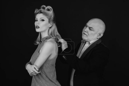 Photo for Young woman with her sugar daddy concept. Capricious beautiful blonde woman in blue dress. Elder man with grey hair adjust necklace for his younger girlfriend. Difference of ages - Royalty Free Image