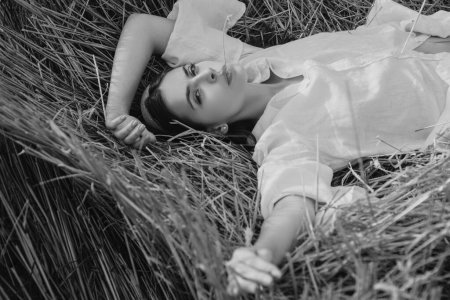 Téléchargez les photos : Jeune agricultrice allongée dans un grenier à foin. Sensuelle fille allongée dans le foin, meule de foin. Portrait de femme dans le champ à la campagne - en image libre de droit