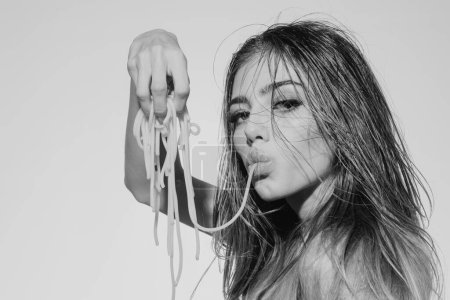 Téléchargez les photos : Femme sensuelle sucer des pâtes spaghetti sur le fond blanc isolé. Portrait studio de mode - en image libre de droit