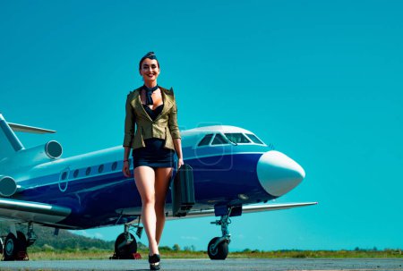 Photo for Full length of airhostess on private jet airplane on airport. Airline. Airplane and woman. Charming stewardess. Attractive flight attendant near airplane in airport. Plane travel - Royalty Free Image
