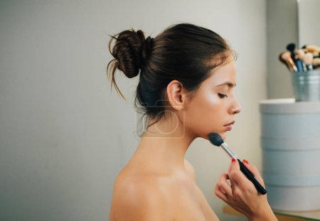 Photo for Visagist is doing professional makeup for cute pretty girl with bare shoulders. Professional makeup artist salon. Beautiful young girl is getting ready by her personal makeup artist - Royalty Free Image