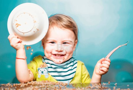 Photo for Cute excited funny baby with plate and spoon, babies eating. Kid boy eating healthy food - Royalty Free Image