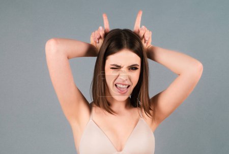 Photo for Young woman doing funny gesture with finger over head as bull horns. Crazy funny sexy girl doing funny gesture with finger over head as bull horns - Royalty Free Image