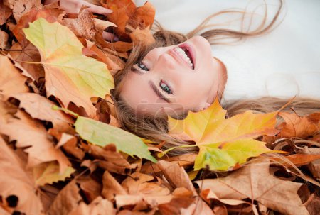 Foto de Mujer acostada sobre hojas de otoño. Retrato de cerca de una hermosa mujer al aire libre - Imagen libre de derechos