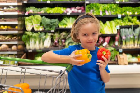 Foto de Niño con verduras y pimientos en la tienda de comestibles. Niño comprando fruta en el supermercado. El niño compra verduras frescas en la tienda de comestibles. Niño eligiendo verduras. Alimento saludable - Imagen libre de derechos