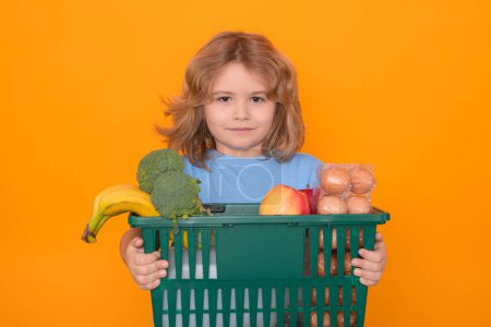 Téléchargez les photos : Magasin d'alimentation. Portrait d'enfant avec panier d'épicerie. Enfant avec panier, isolé sur fond de studio jaune - en image libre de droit