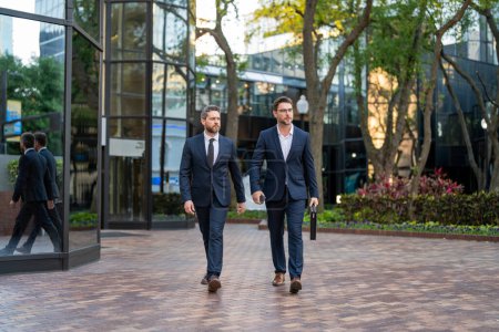 Photo for Businessmen talking on city street. Two colleagues business men walking outdoors on the street. Cheerful business conversation. Two businessmen walking outside business center, having conversation - Royalty Free Image