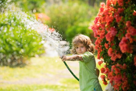 Foto de Niños regando flores y plantas en el jardín. Niño con manguera de agua en el patio trasero. Jardinería para niños. Niños verano diversión al aire libre en casa - Imagen libre de derechos