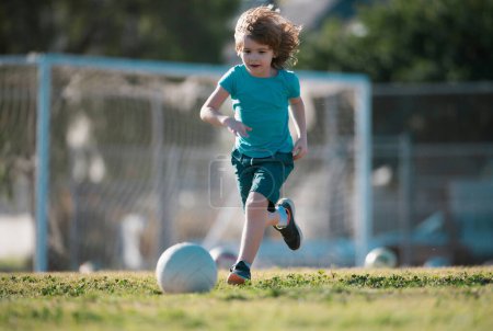Téléchargez les photos : Petit garçon courir et jouer au football sur le terrain avec le ballon de football. Concept de sport pour enfants. Enfance et sport. Petit champion de football - en image libre de droit