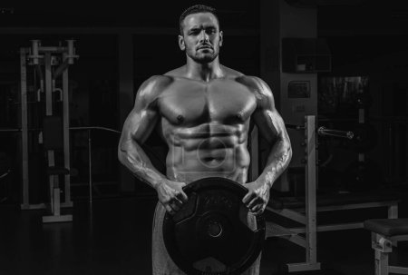 Téléchargez les photos : Powerlifter avec disque de poids lourd dans la salle de sport. bodybuilder formation son biceps - en image libre de droit