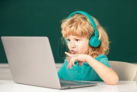 Téléchargez les photos : Garçon portant des écouteurs, étude avec ordinateur portable en classe, cours de leçon audio écoute - en image libre de droit